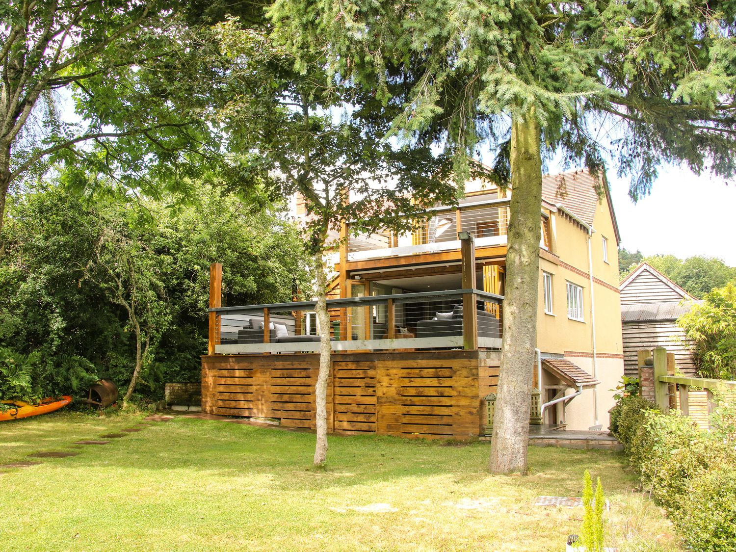 A wooden deck with outdoor furniture attached to a yellow house with trees and grass around Sunnyside Bircher Common near Yarpole