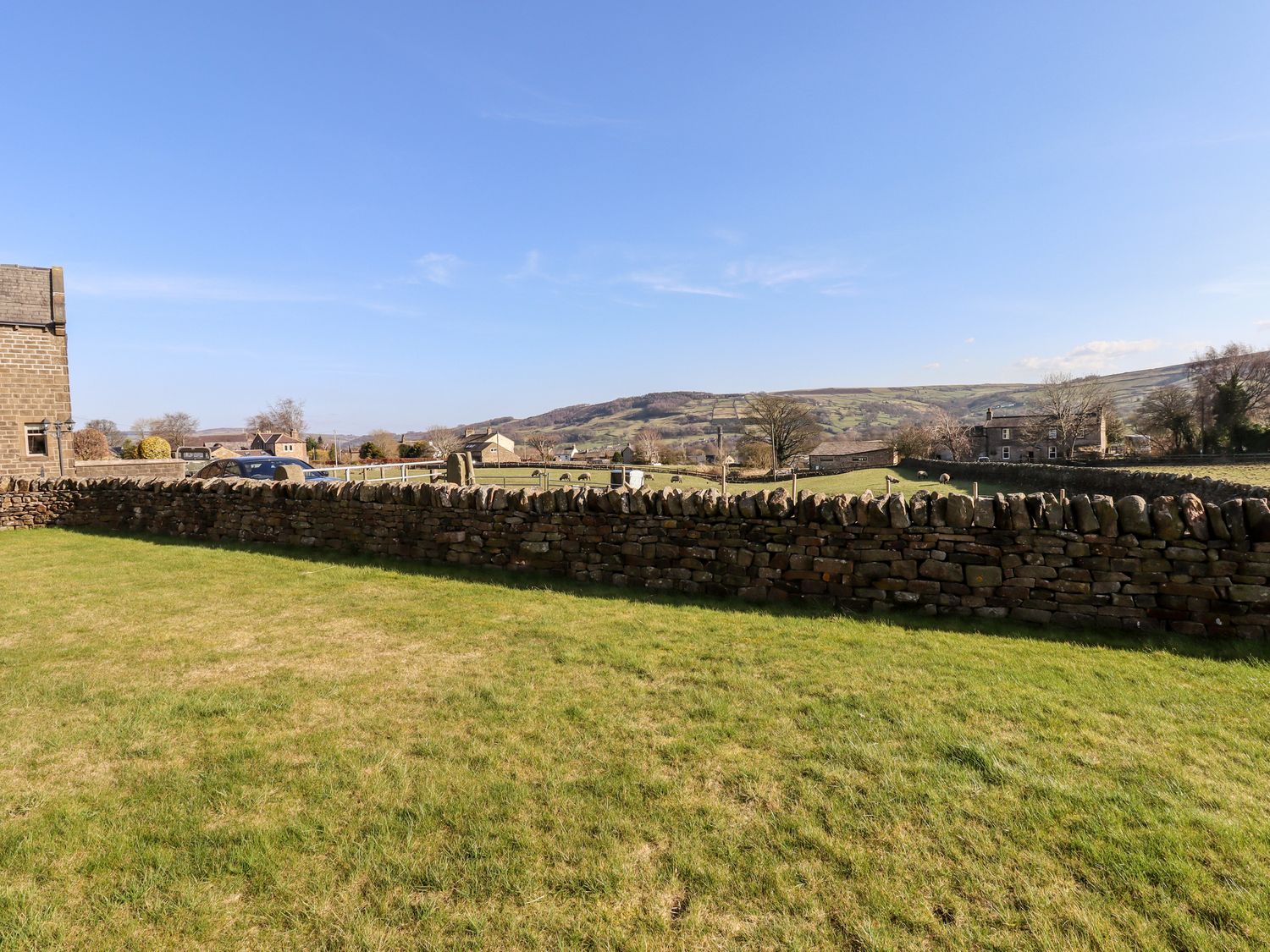 A grassy backyard with a stone wall and countryside view at The Annexe in Glusburn near Skipton
