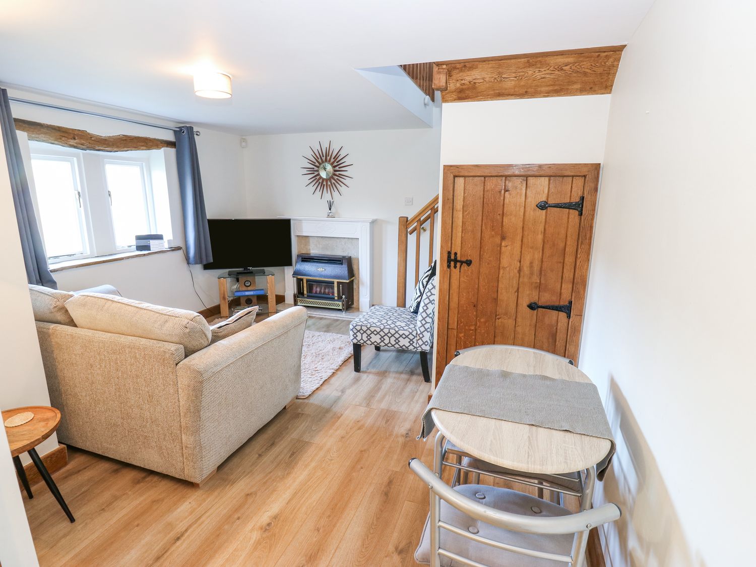 A living room with a sofa, armchair, television, fireplace, dining table, wooden door and window at The Annexe in Glusburn near Skipton