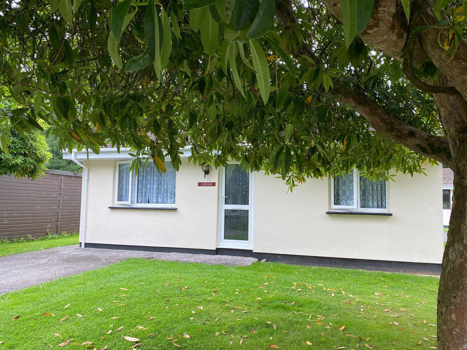 A small house with two windows and a door surrounded by grass and a tree at Lands End in Liskeard near St Cleer