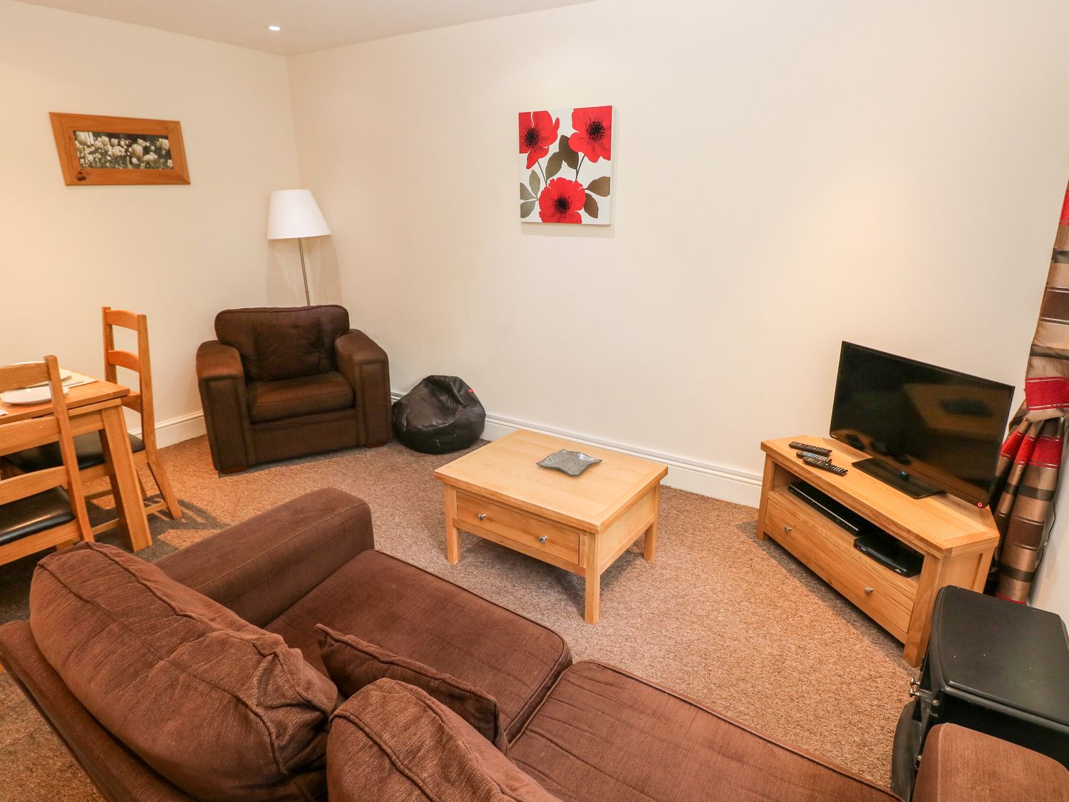 A living room with brown sofas a wooden coffee table a tv on a wooden stand and a dining table with chairs at Swallows Cottage in Maenclochog