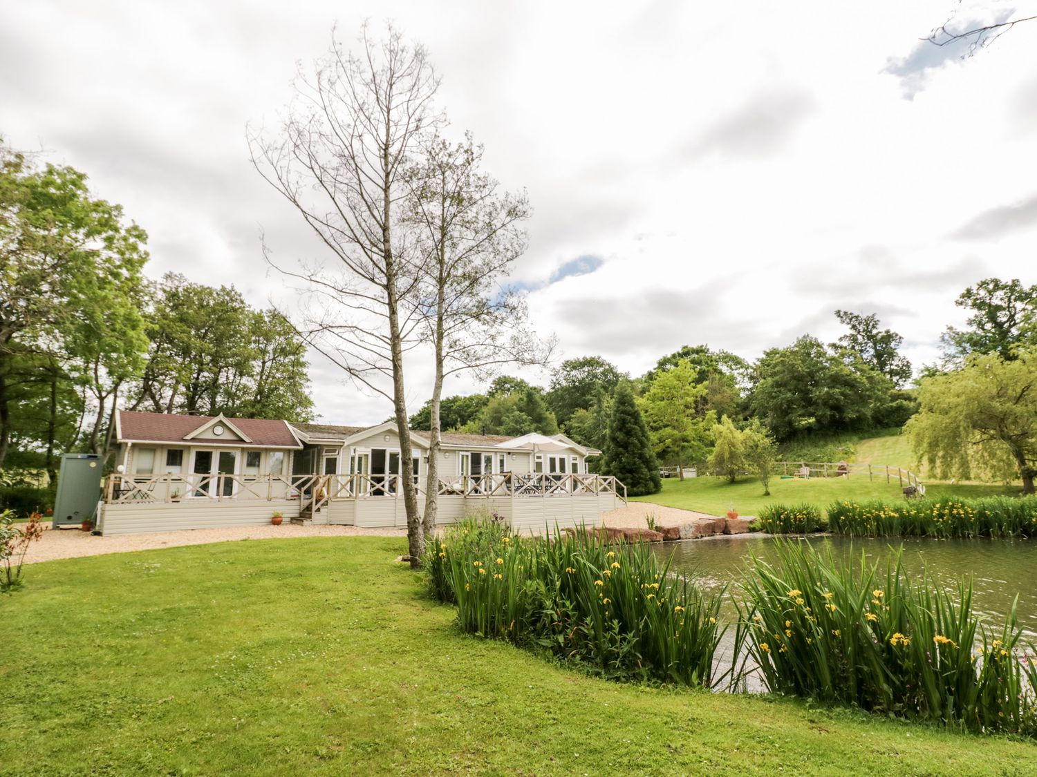 A house with a deck near a pond surrounded by grass and trees at Phocle Lodge in Ross-On-Wye