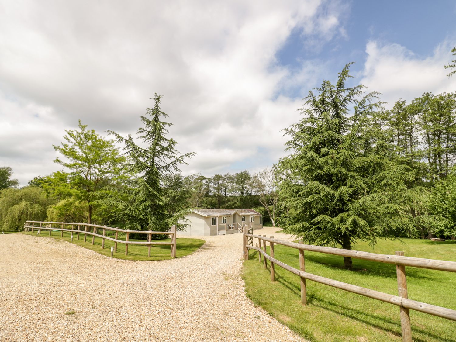 A gravel driveway lined with wooden fences leading to a building surrounded by trees and grass at Phocle Lodge in Ross-On-Wye