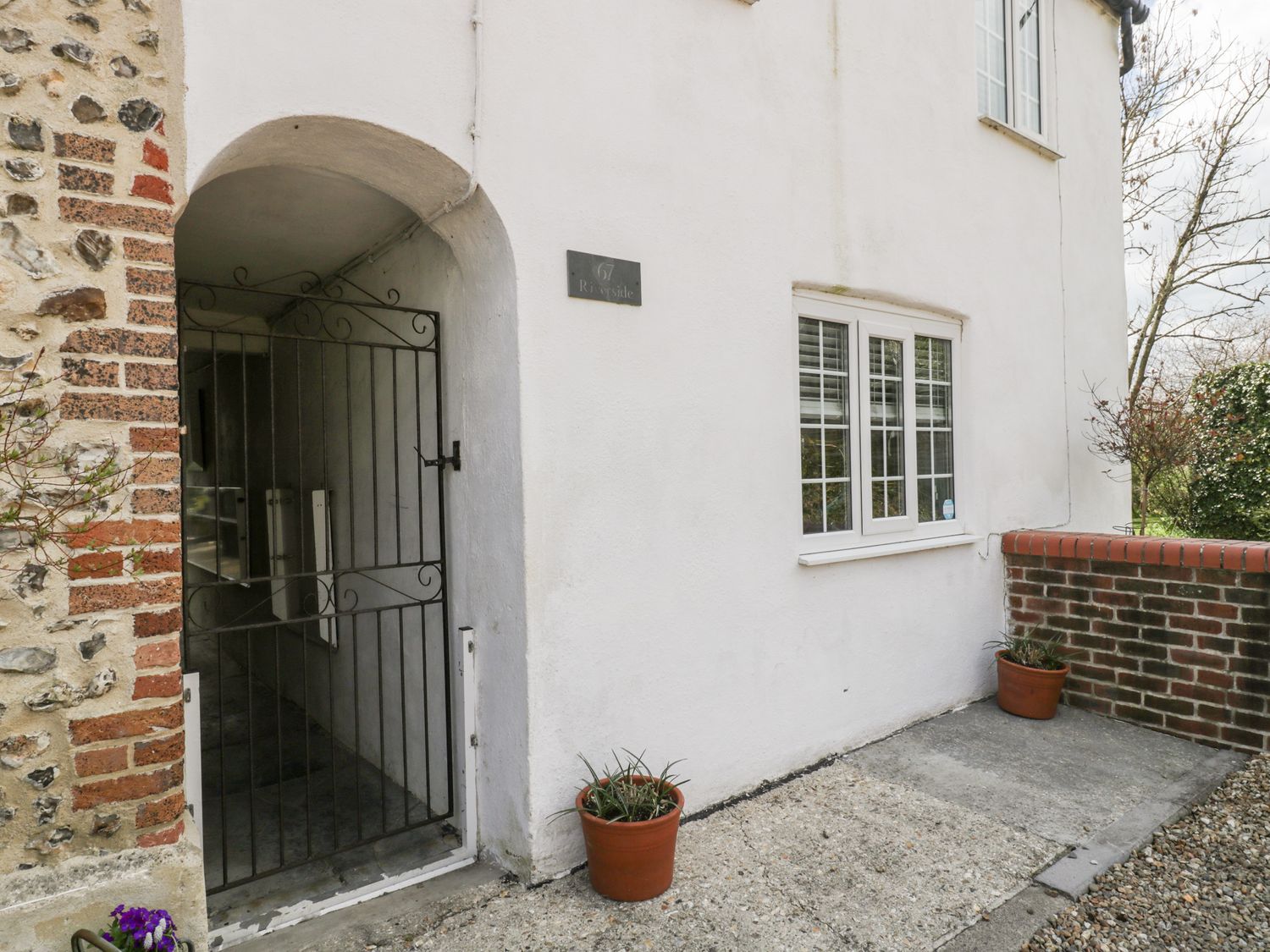 Entrance of a white building with a black metal gate two potted plants and a window at Riverside 67 Dorchester Road in Maiden Newton