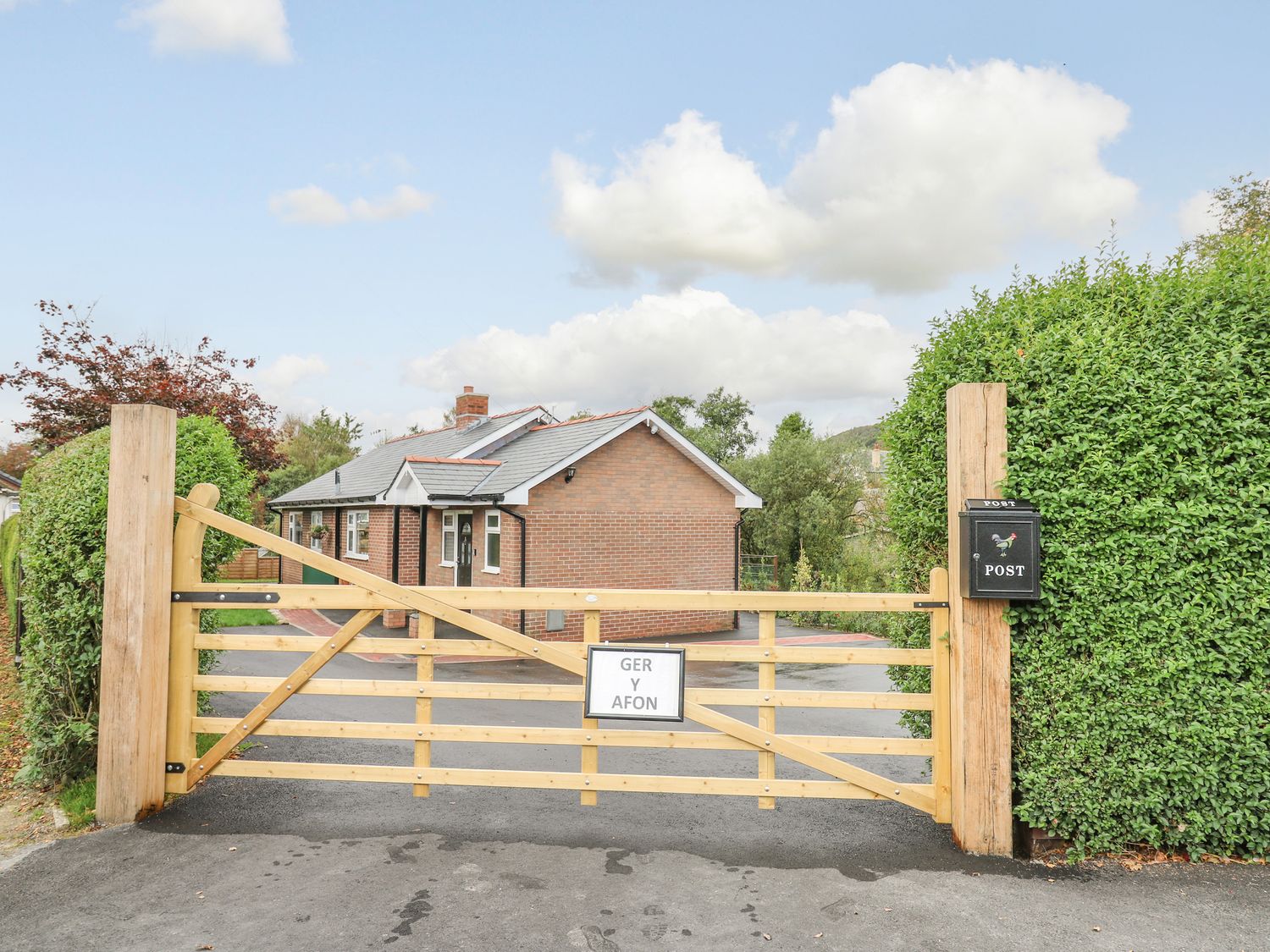 A wooden gate with a sign at the entrance of a brick house with a hedge and a mailbox at Ger Yr Afon Cottage in St Harmon near Rhayader
