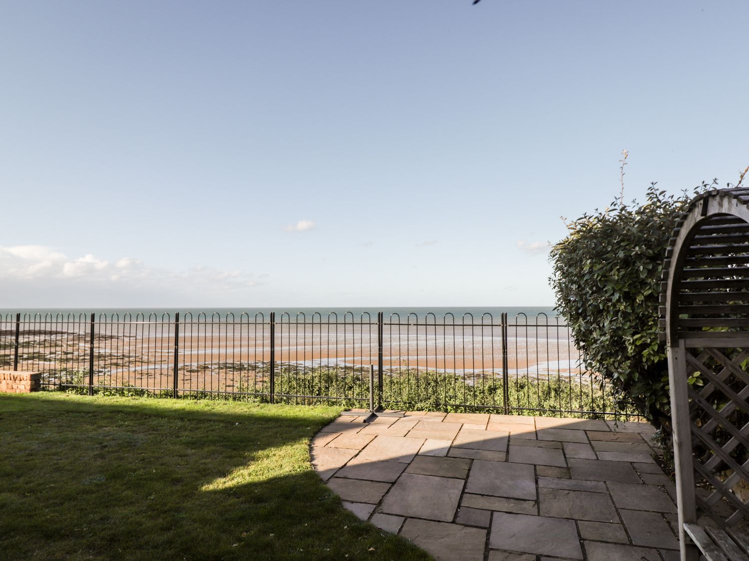 A garden with a metal fence overlooking a beach and ocean at 17 St Magnus Close in Birchington On Sea