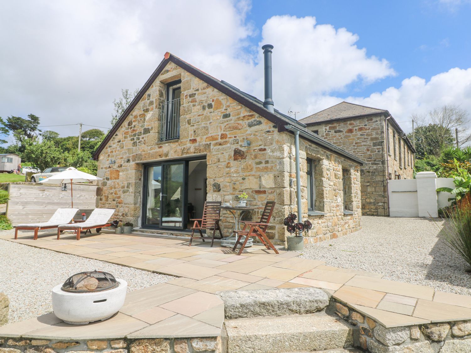 An outdoor patio with loungers chairs and a fire pit next to a stone house at Apple Blossom Barn in Gulval near Penzance