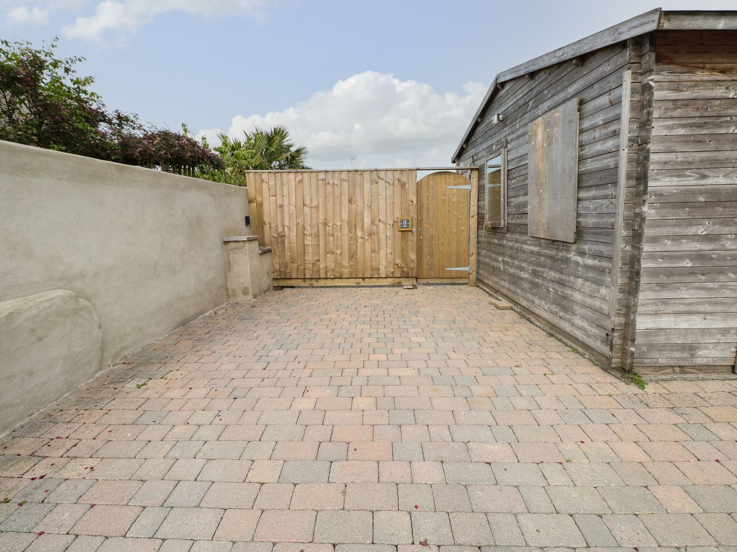 A paved courtyard area with a wooden gate and a wooden shed at Holly Cottage in Pembroke