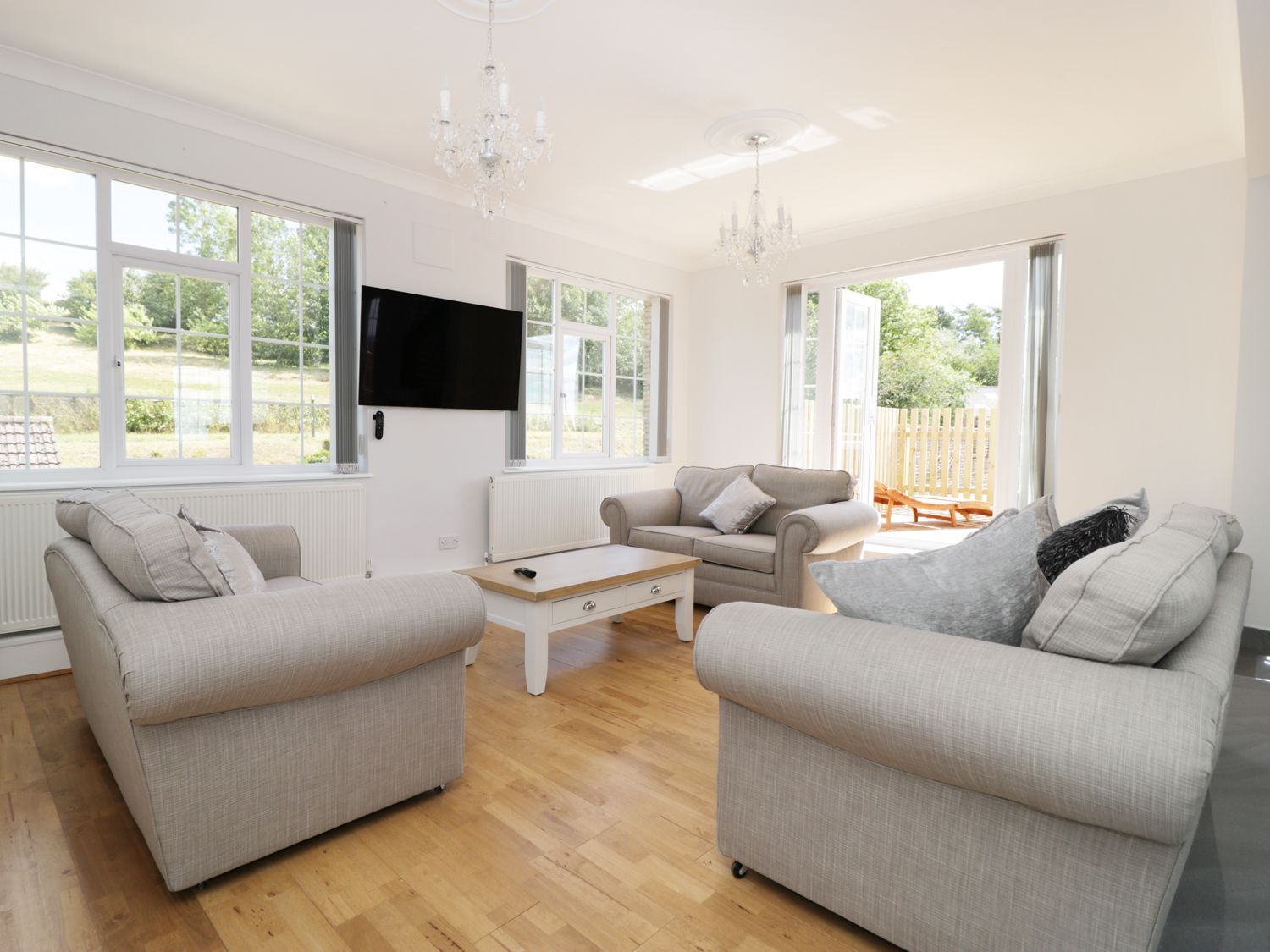A living room with three grey sofas a wooden coffee table two chandeliers and a wall-mounted TV at Castle Top Retreat in Nettleton Lincolnshire