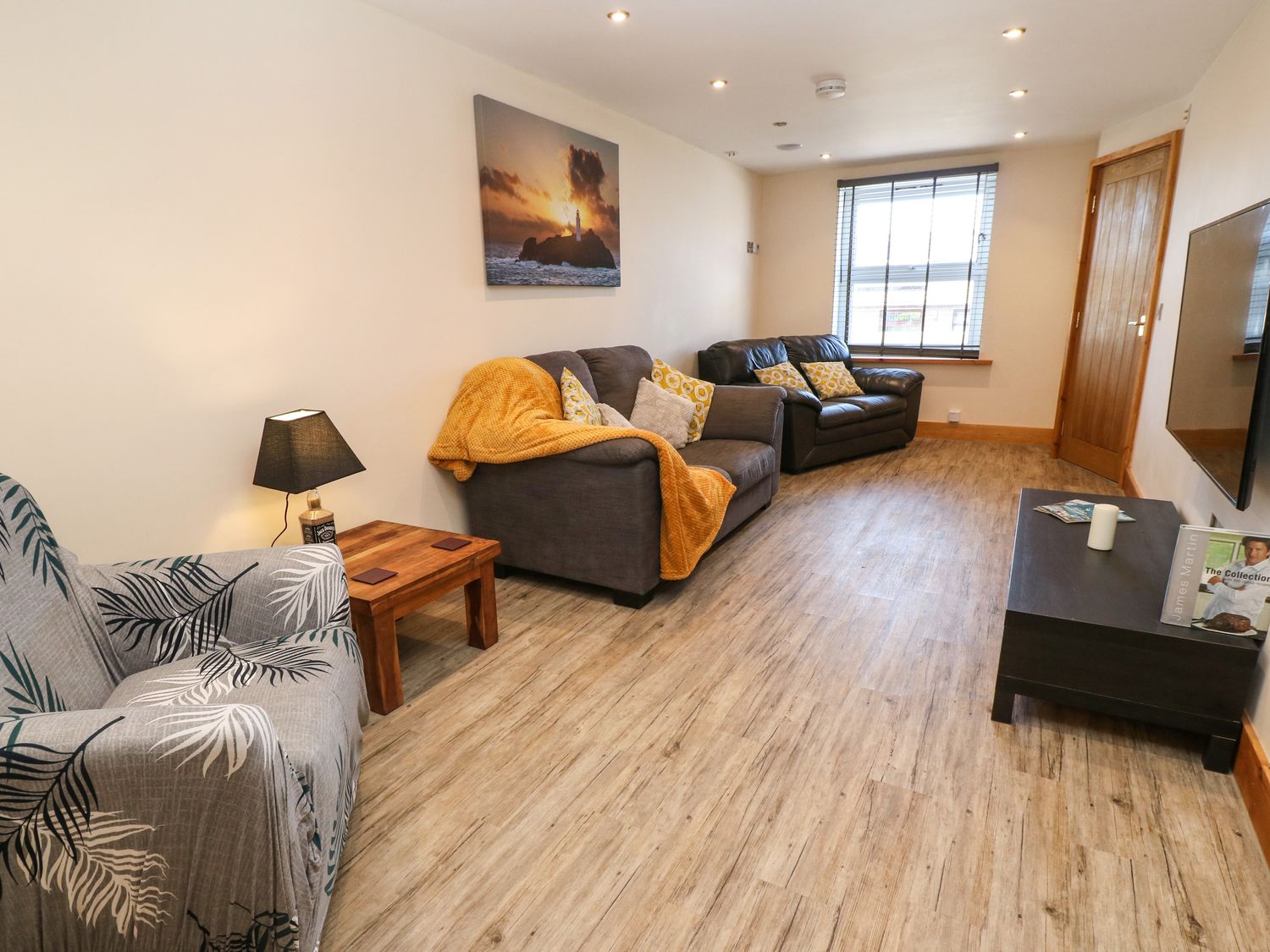 A living room with two sofas armchair wooden coffee table lamp wall art and a window at Godrevy Cottage in Hayle