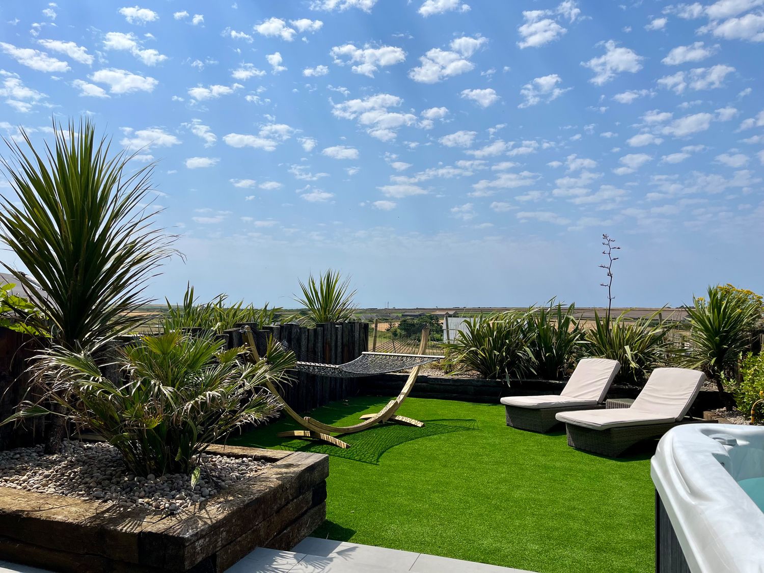 An outdoor patio with a hammock two lounge chairs various plants and a hot tub at Sea Scape in Sennen
