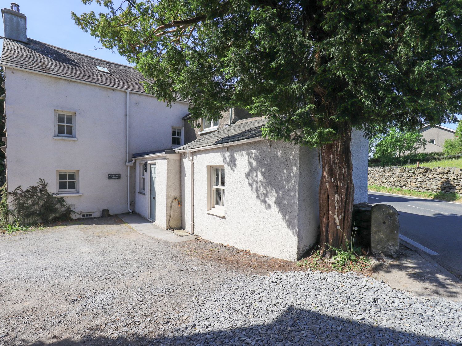 An exterior view of a house with a tree and gravel area at Bridge End Cottage Haverthwaite near Cartmel