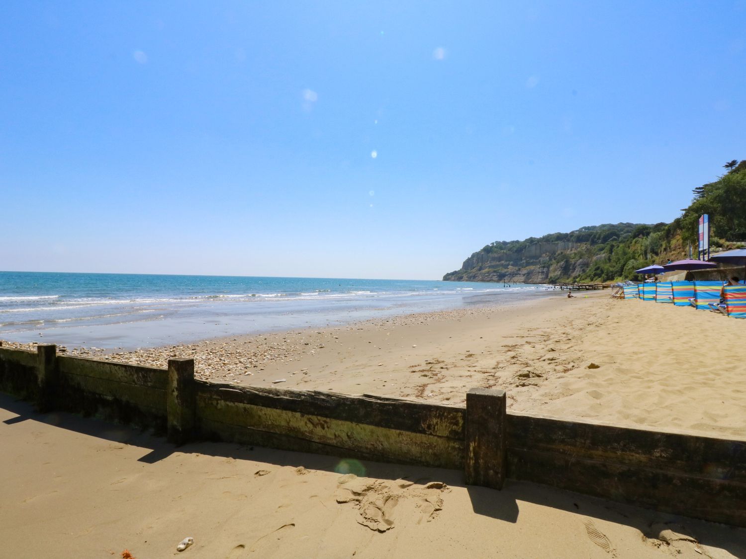 A sandy beach with waves and a wooden barrier near cliffs and beach umbrellas at Pilgrim's Loft in Ventnor