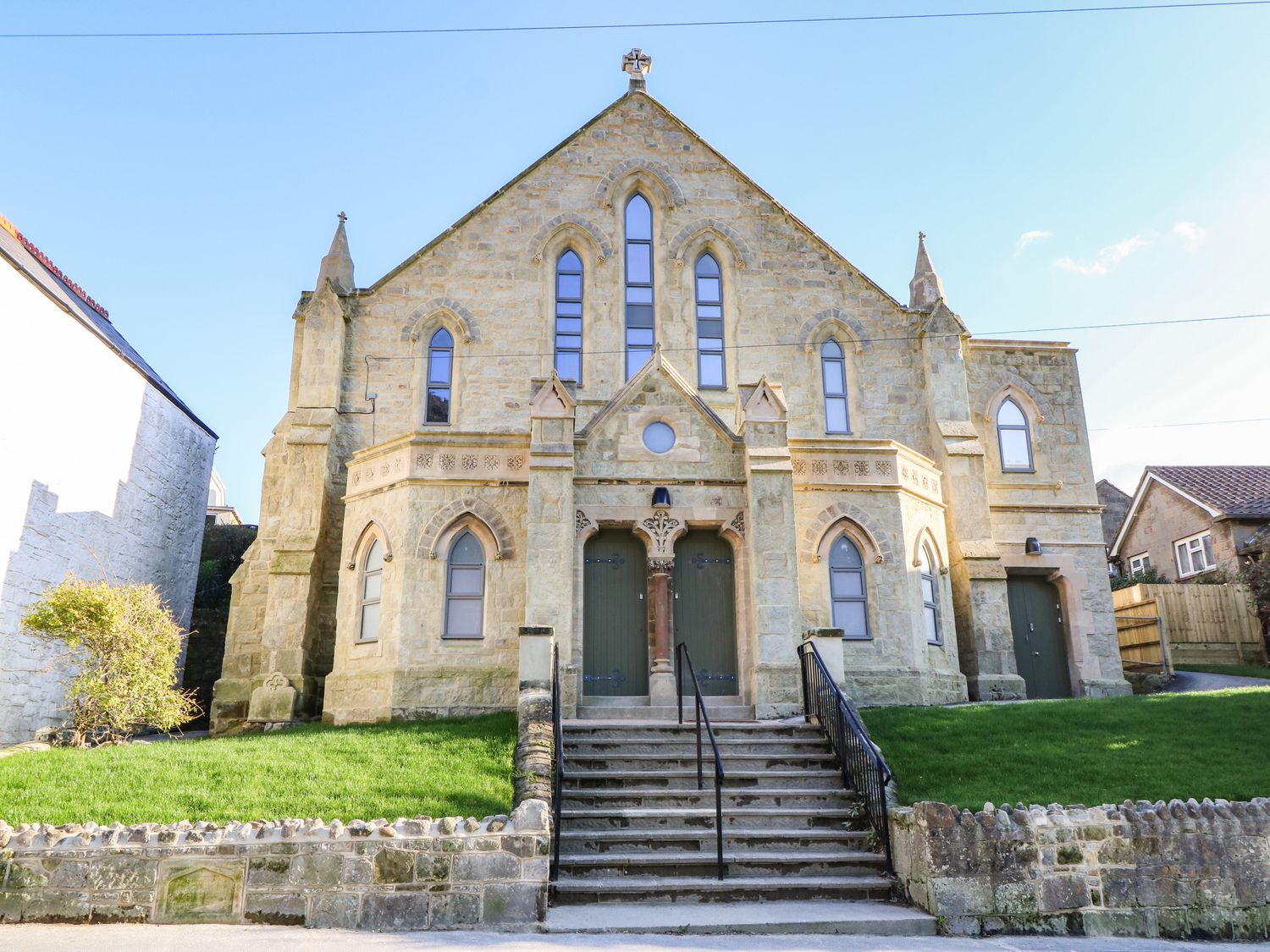 Stone building with arched windows and two green doors at the top of stairs with grass on both sides