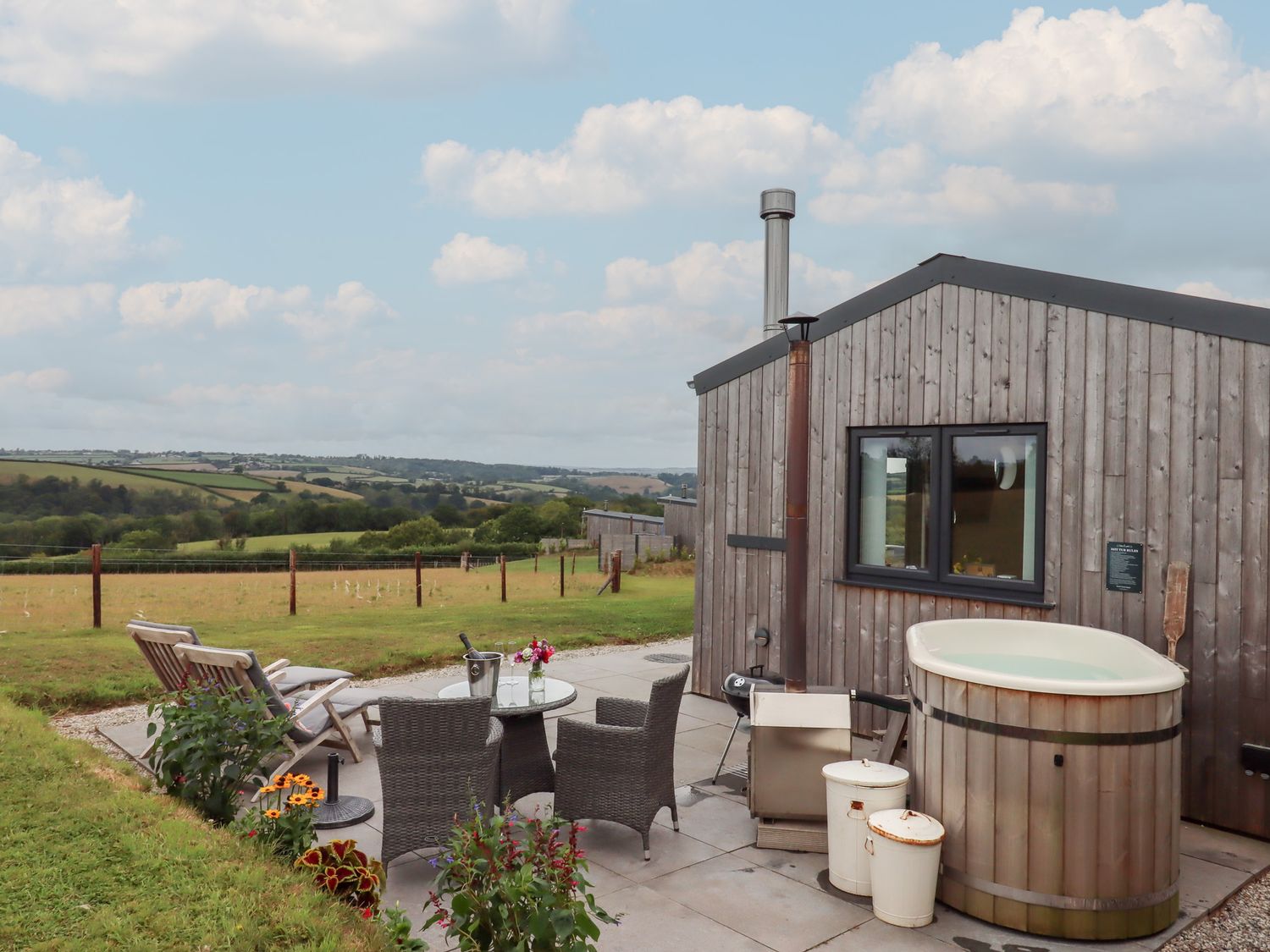 An outdoor area with a wooden cabin, hot tub, table and chairs at The Pennymoor Cadeleigh near Tiverton