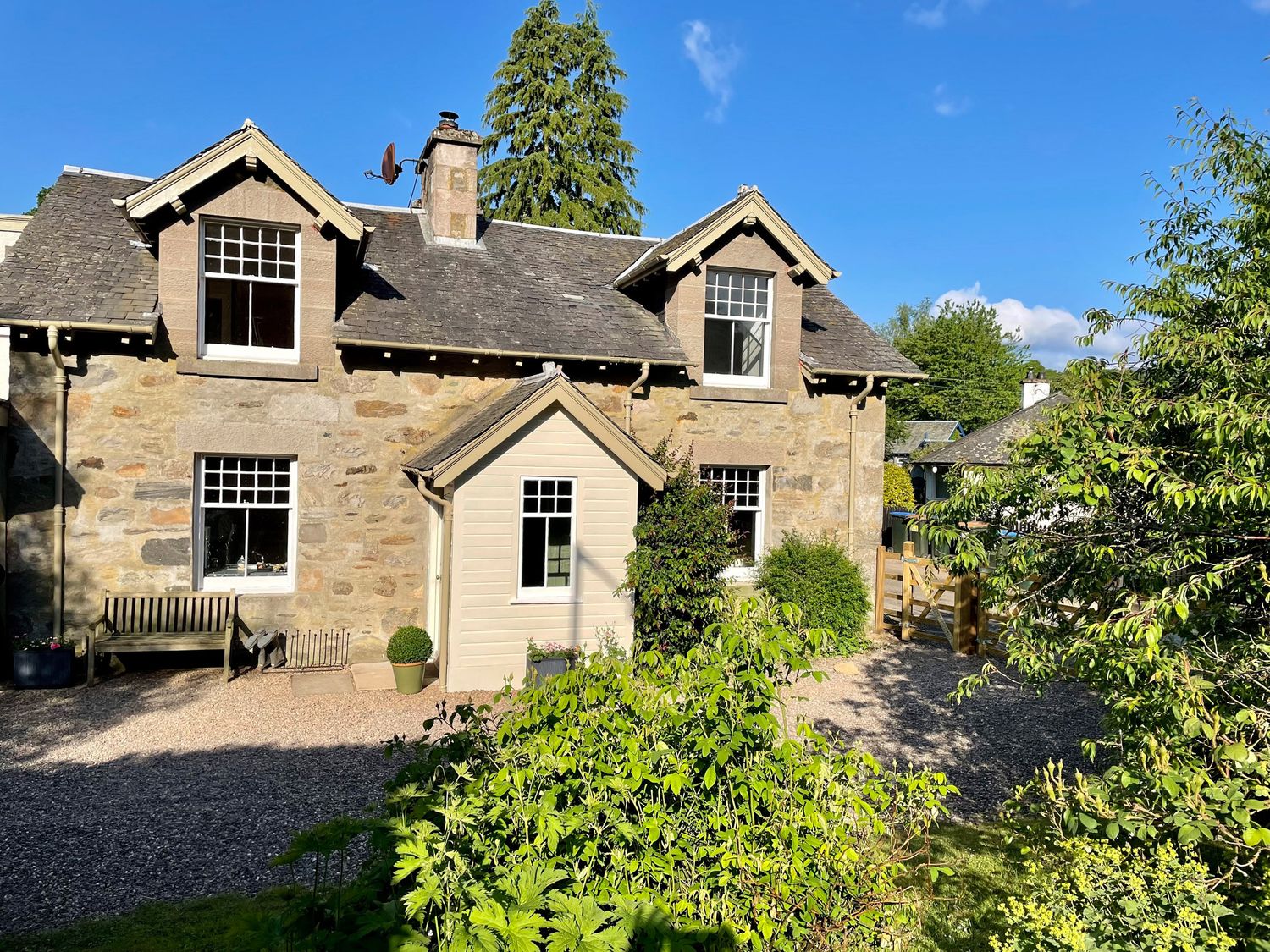Stone house with wooden porch and bench surrounded by plants and gravel at Old Schoolhouse in Grandtully