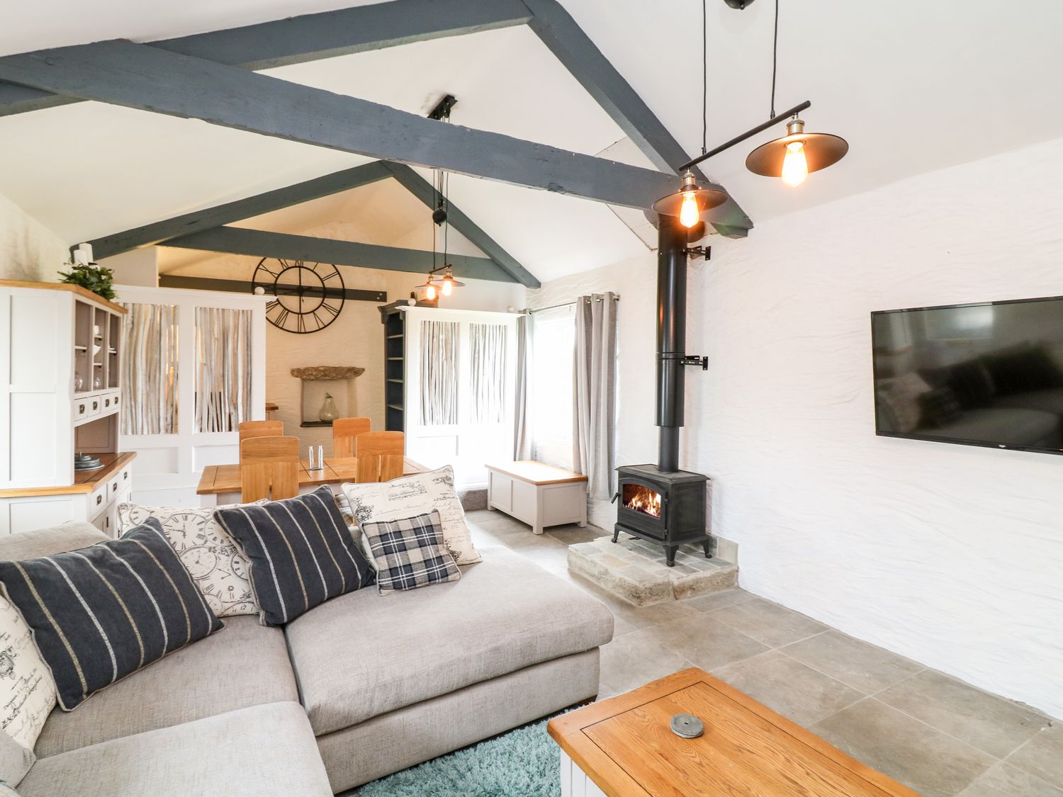 A living area with a sectional sofa dining table wood burning stove and mounted television at Polgear View Polgear Nr Redruth