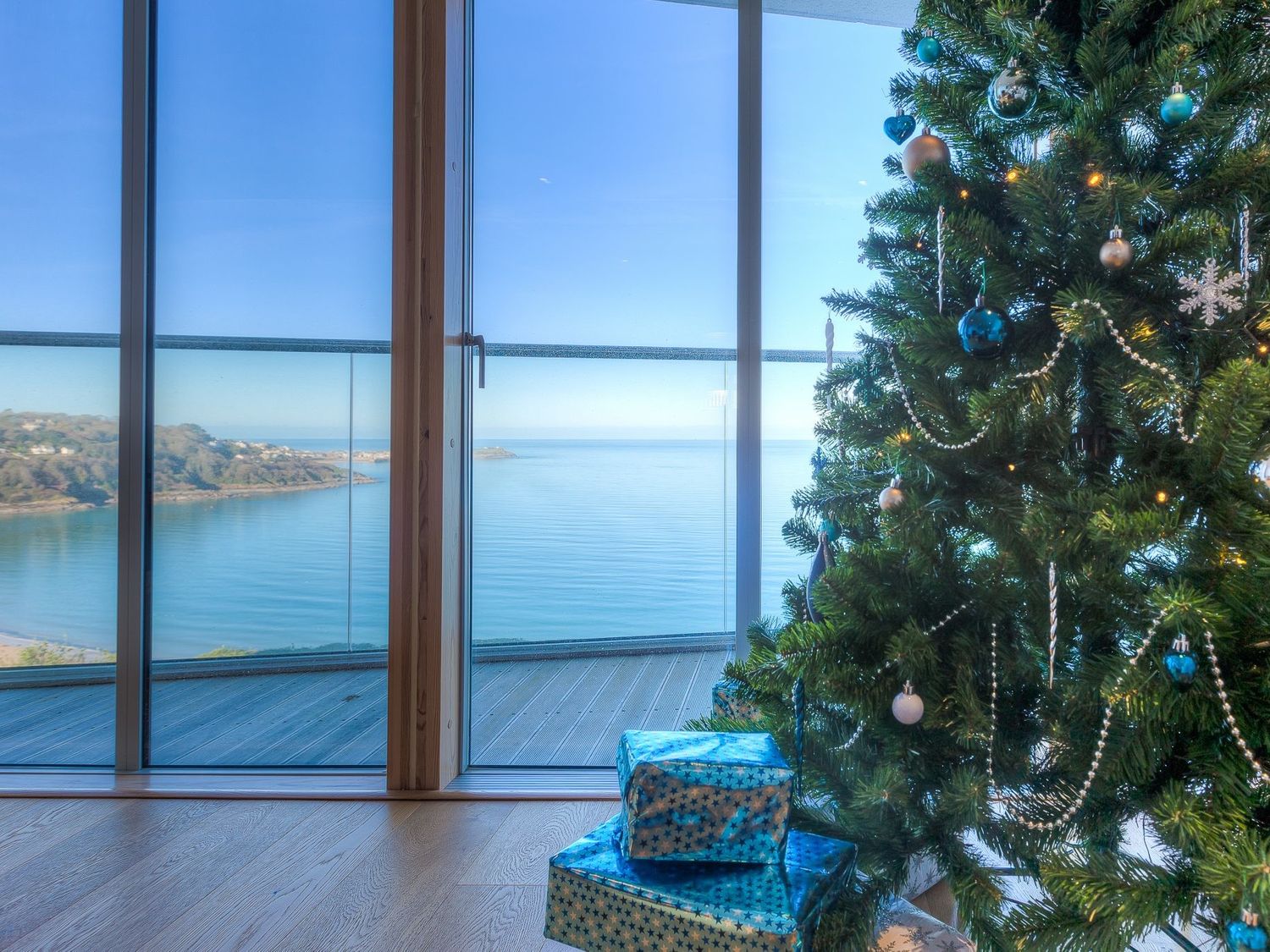 A room with a decorated Christmas tree and wrapped presents by a window overlooking a coastal view at Kittiwake in Carbis Bay