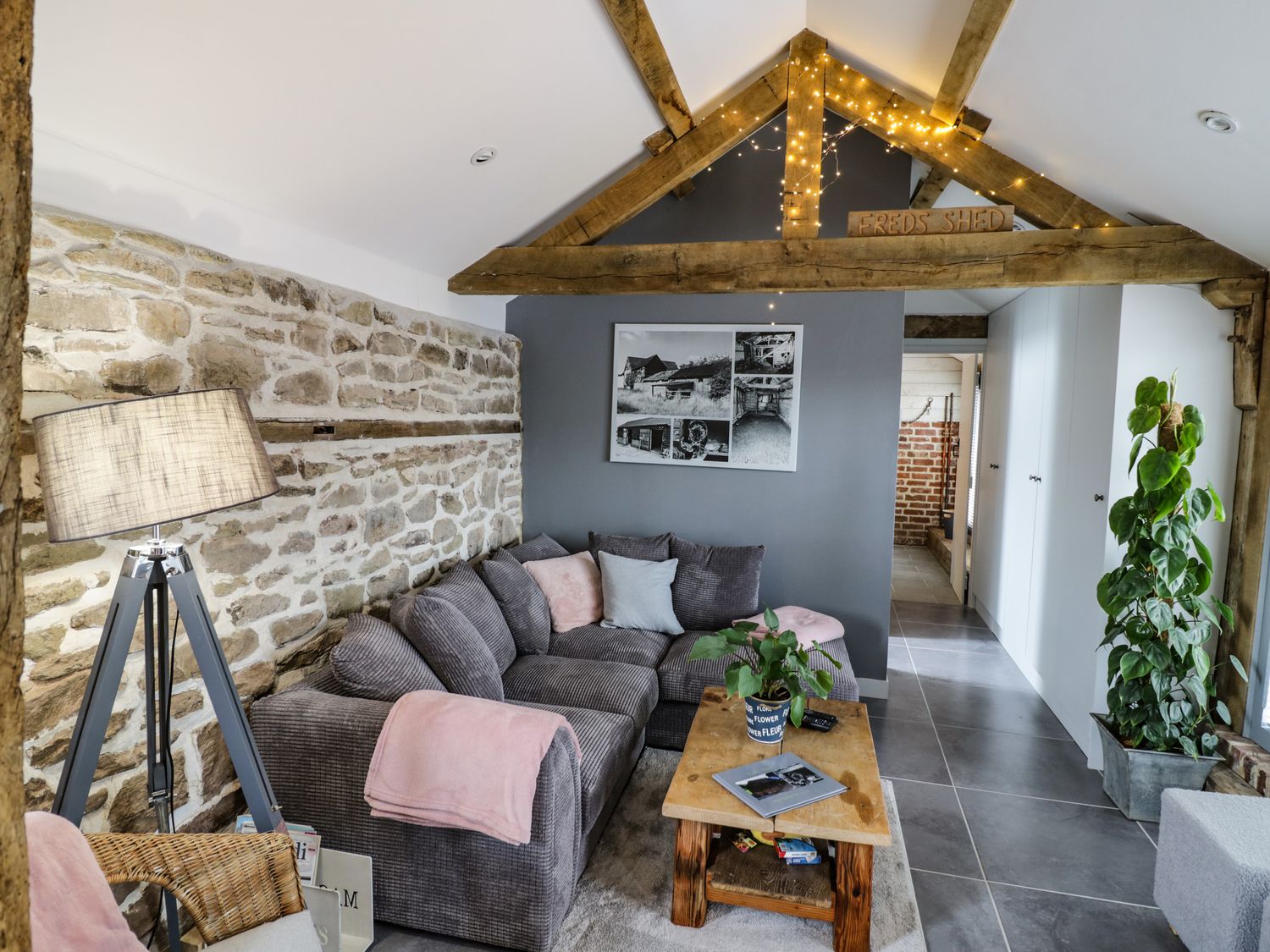 A living room with a gray sofa a wooden coffee table a floor lamp and a plant at Freds Shed in Hereford