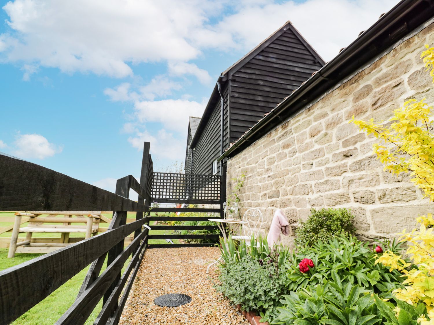 A small garden area with a gravel path and green plants next to a stone wall and black wooden fence at Freds Shed in Hereford
