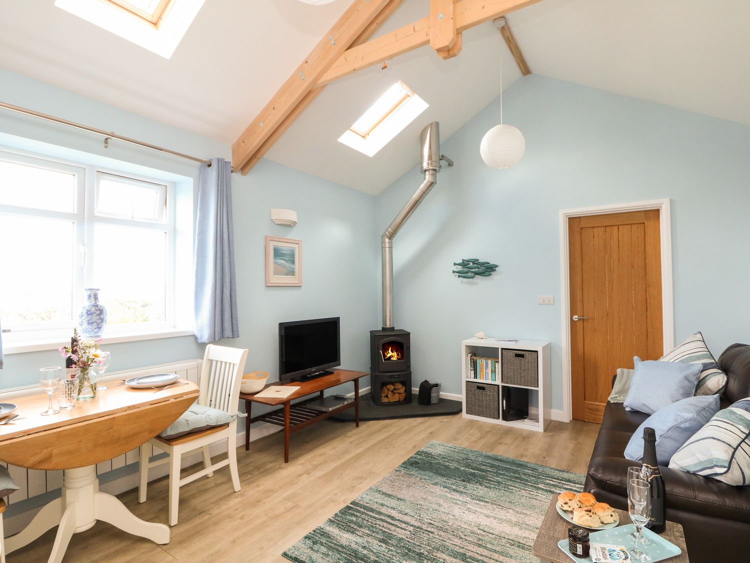 A living room with a wood stove a dining table and a sofa at Driftwood Kelynack near St Just