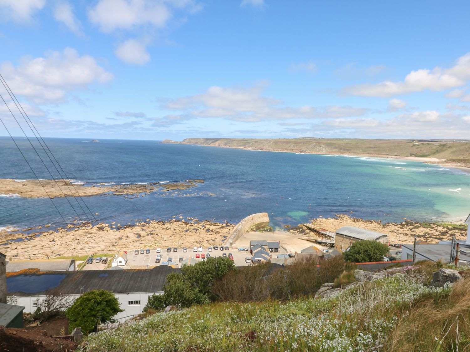 A coastal view showing a rocky shore parking area buildings and a sea wall at Driftwood in Kelynack near St Just