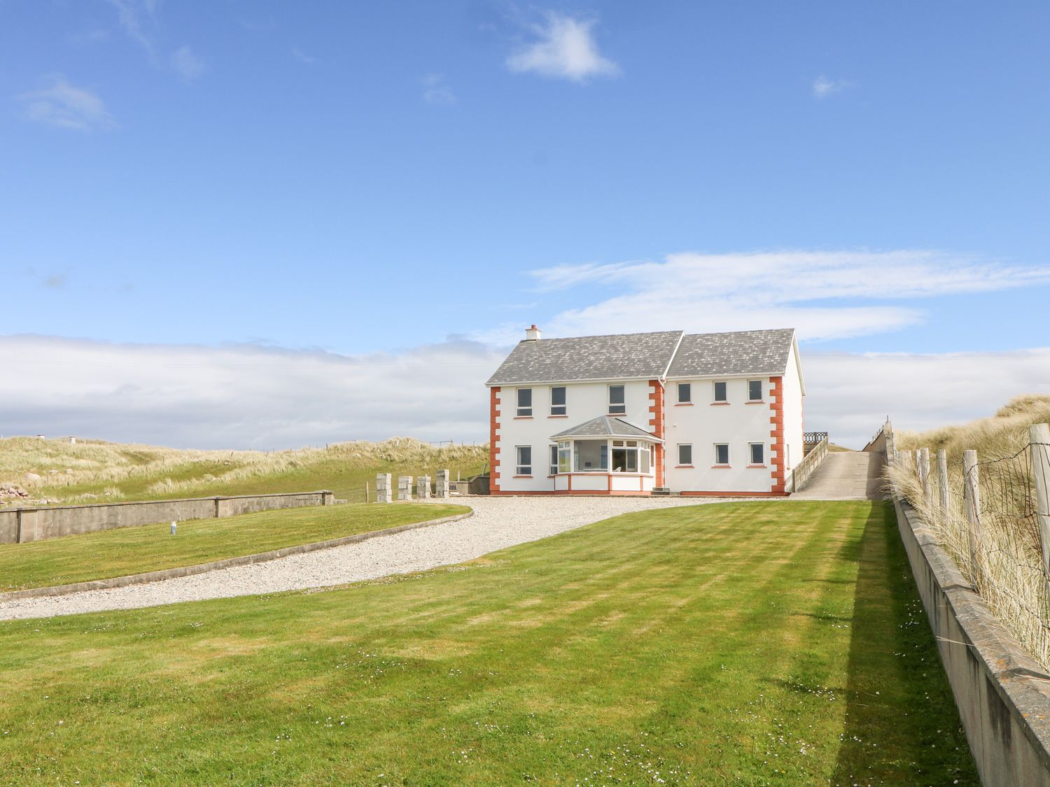 A large white house with red trim at the end of a gravel driveway surrounded by grass at Realt na Farraige in Derrybeg County Donegal
