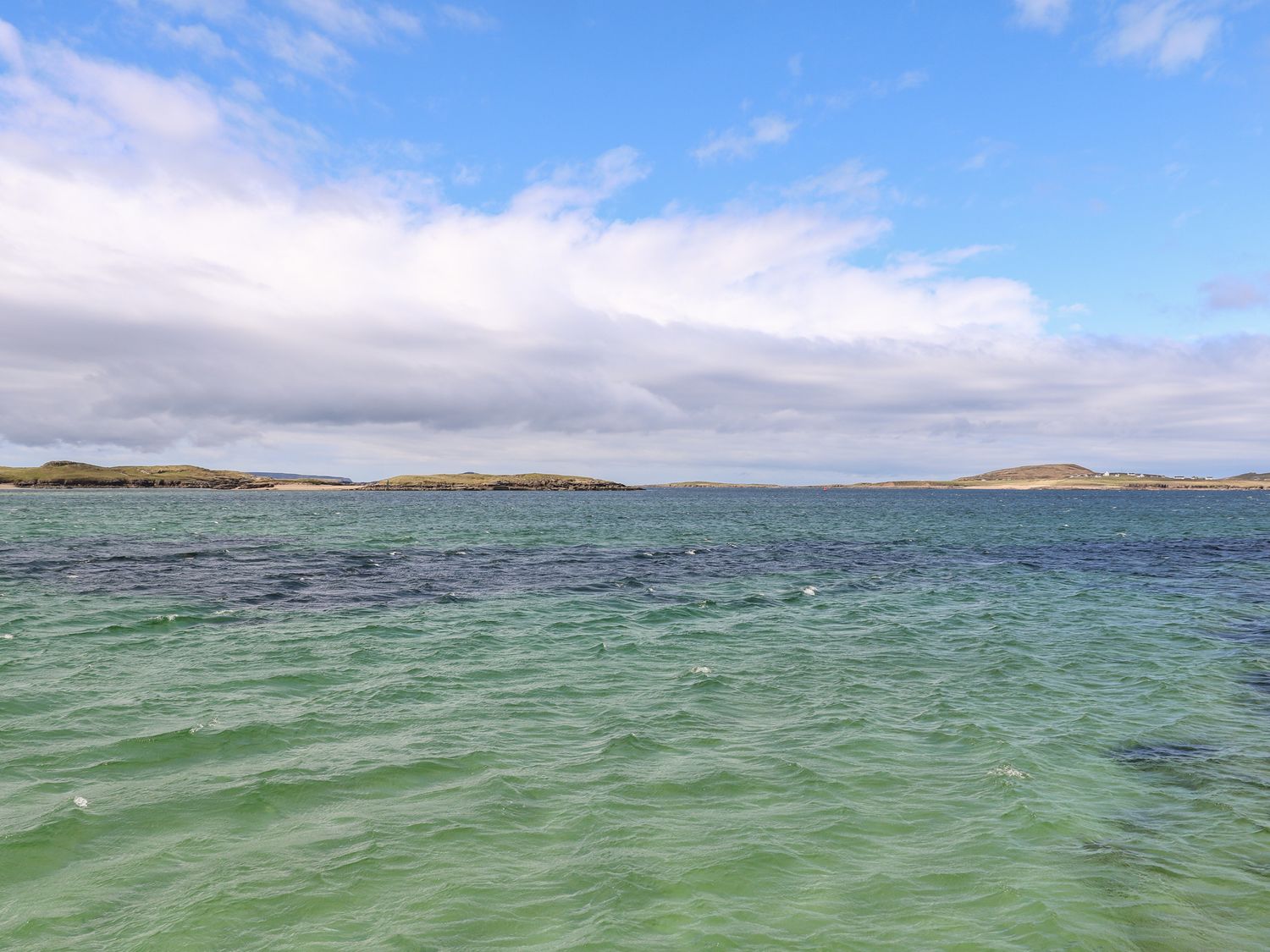 A coastal view of water with small islands and a partly cloudy sky at Realt na Farraige in Derrybeg County Donegal