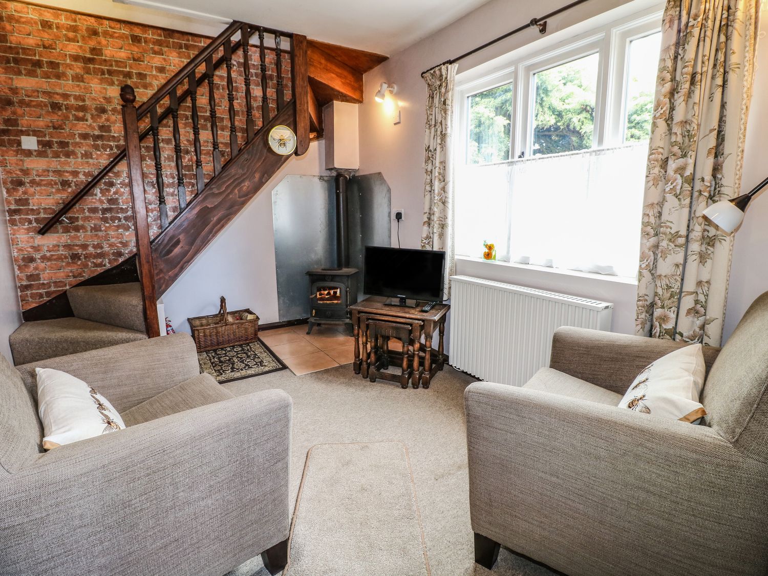 A sitting room with two armchairs a television on a wooden stand a wood-burning stove and a staircase at The Mill Wheel in Doveridge