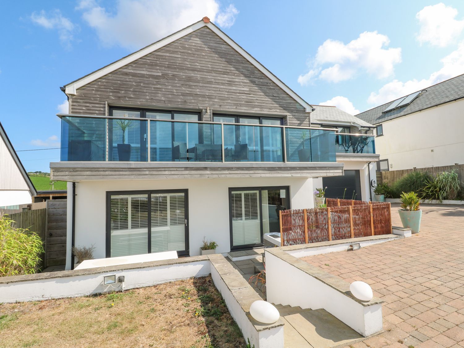 A two story house with glass balcony and patio area at Sandbanks in Praa Sands
