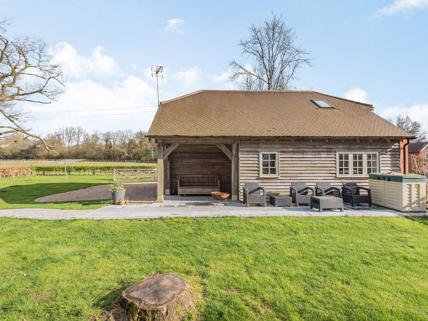 A wooden building with a covered porch bench patio furniture and green grass in a rural setting at Red Kite Cottage in Froxfield Hampshire