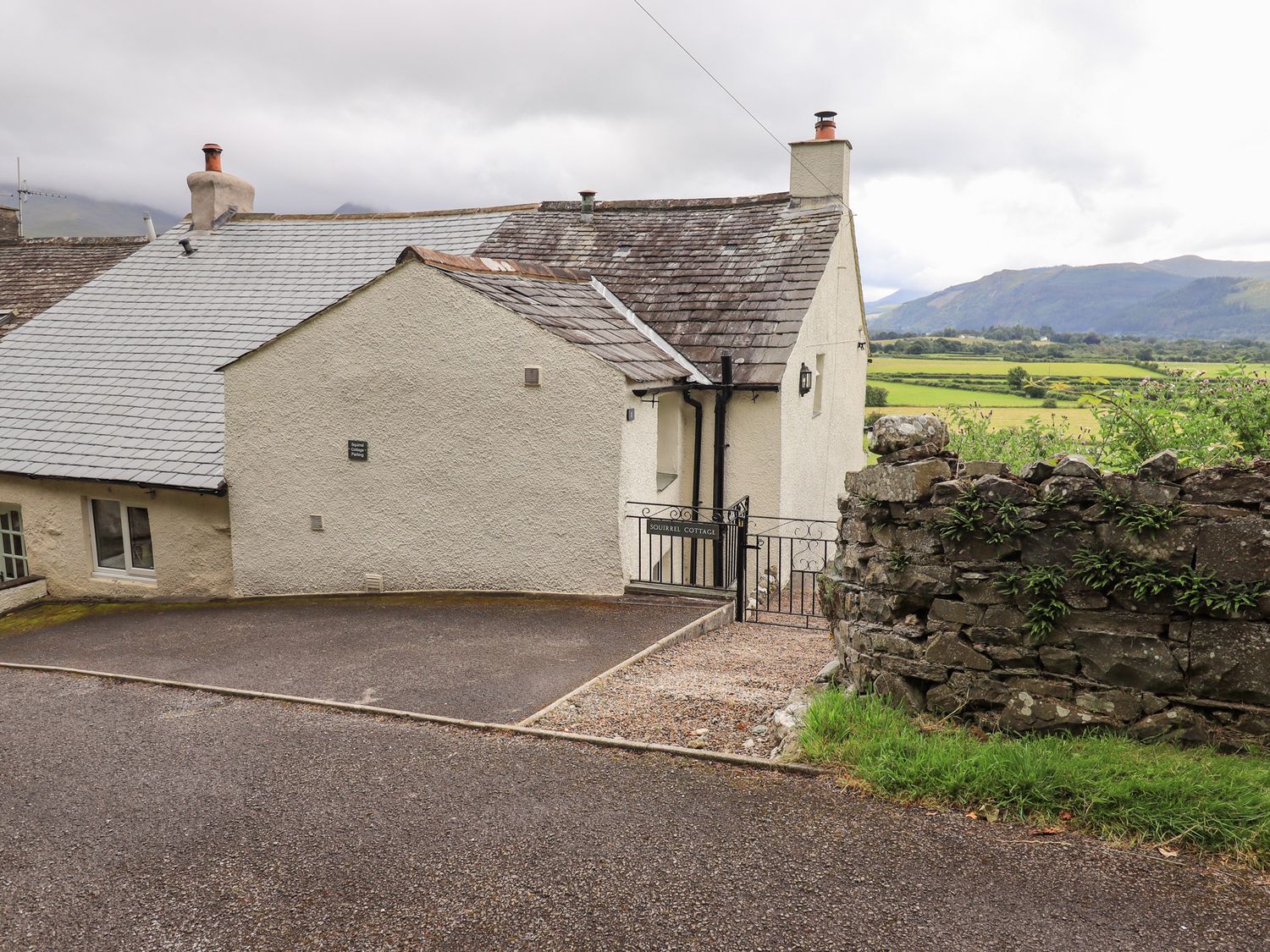 Exterior view of a house with a stone wall and driveway at Squirrel Cottage in Bassenthwaite