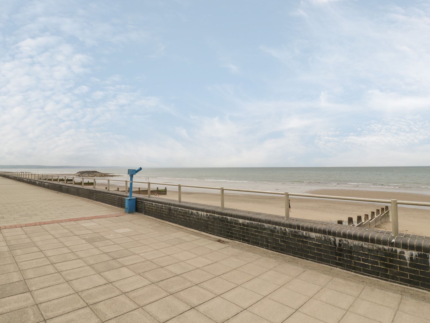 A beachfront promenade with railing and a blue viewing scope overlooking the sandy beach and sea at The Nook in Tywyn