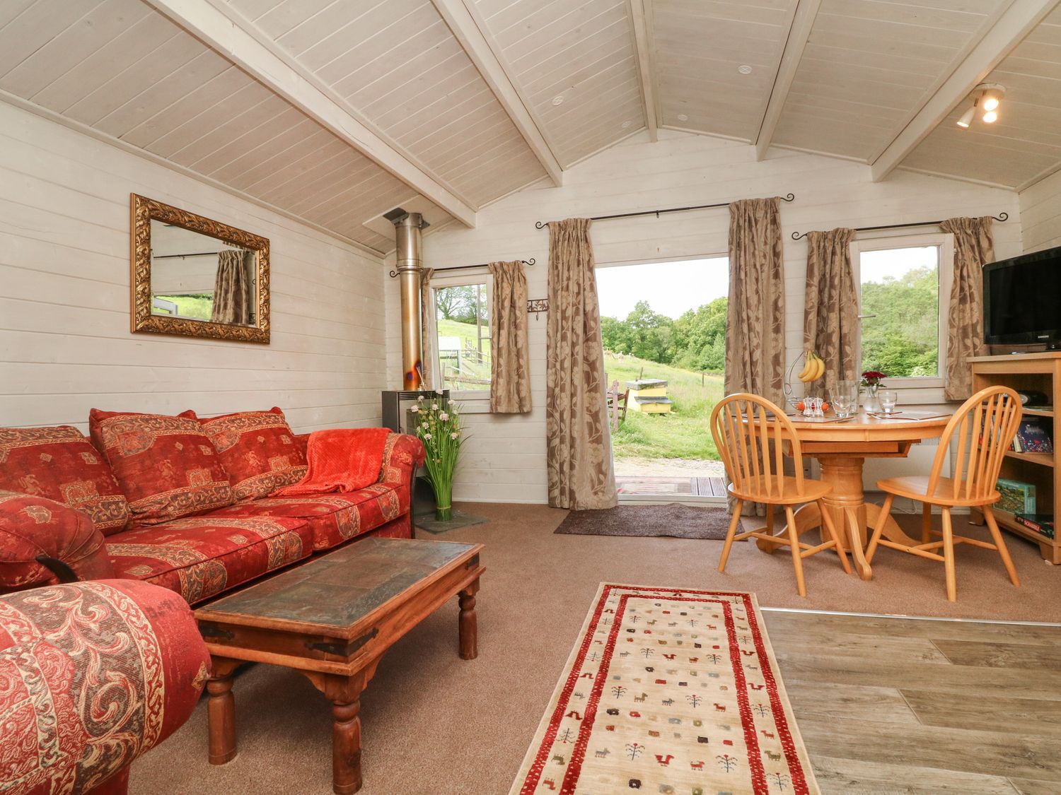 A living room with red patterned sofa wooden coffee table round wooden dining table and chairs at The Cabin Lowley Brook Farm Rezare near Launceston
