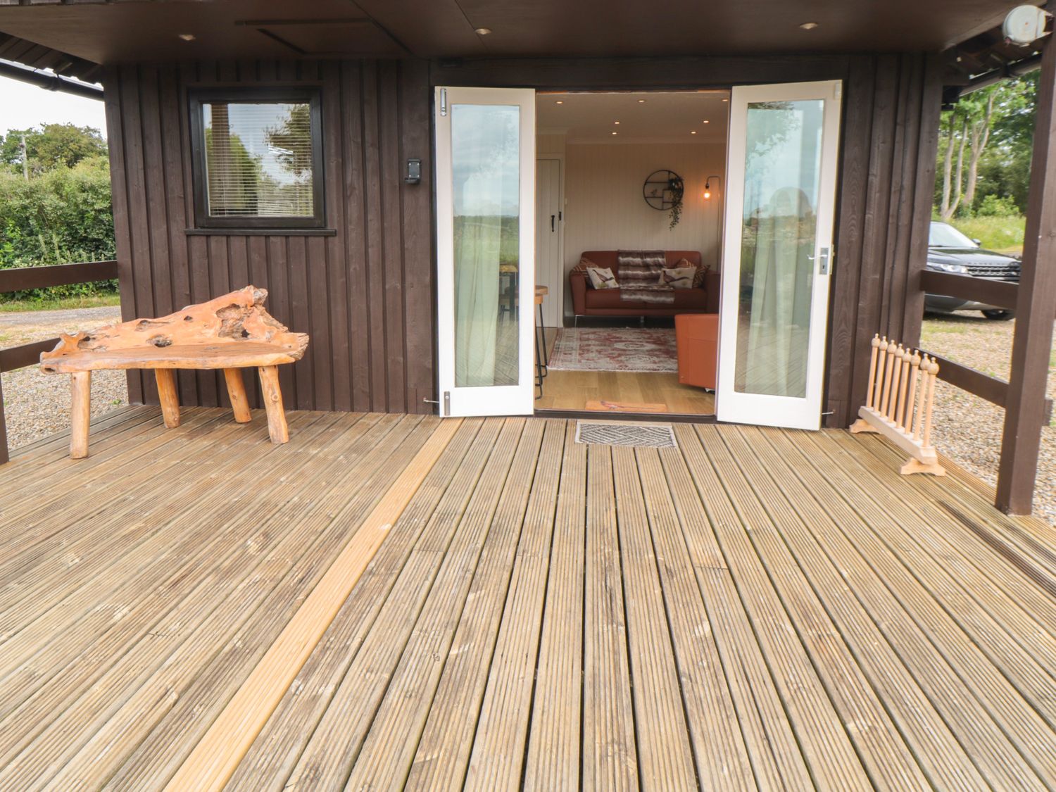 A wooden deck with a natural wood bench outside doors leading to a living room at 3 Valley View Lodges in Nawton near Helmsley