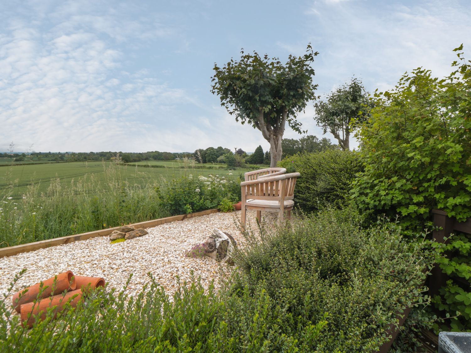 A garden area with a wooden bench surrounded by bushes and trees overlooking green fields at 3 Valley View Lodges in Nawton near Helmsley