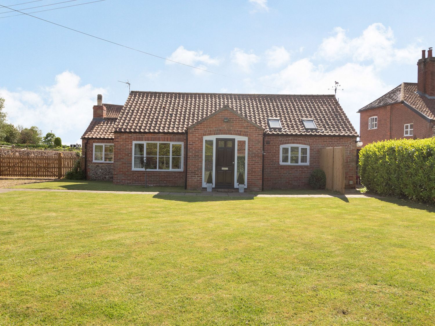 A brick house with a tiled roof and green lawn in front at The Croft in Thompson near Watton