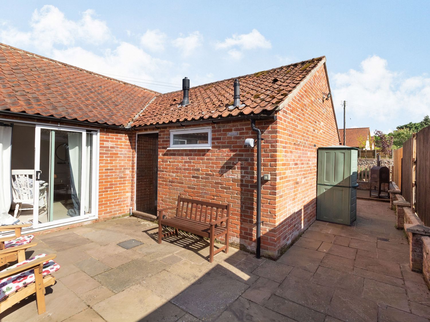 A paved outdoor patio area with wooden bench and chairs next to a brick building at The Croft in Thompson near Watton