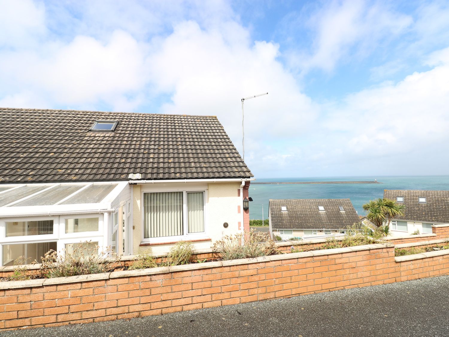 A semi detached house with a sloped tiled roof and a brick wall in front overlooking the sea at Murmur y Mor in Fishguard