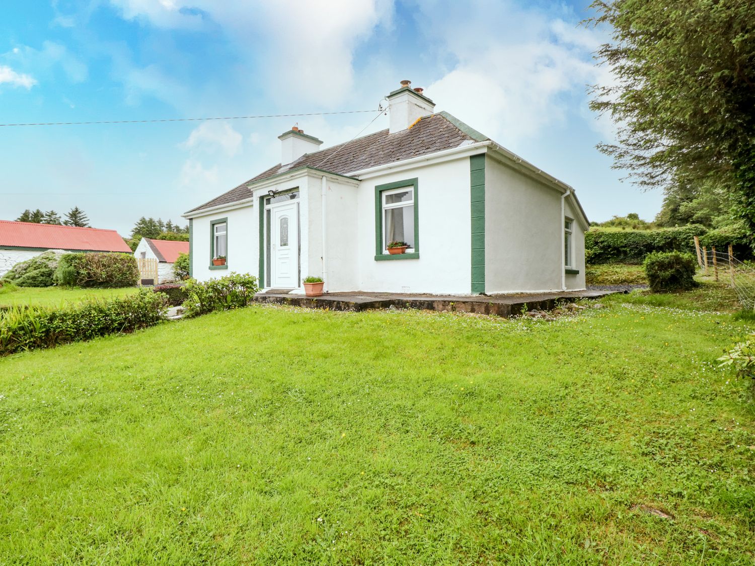 A white single-story house with green trim surrounded by grass and trees at Sean Bhaile in Glenisland near Castlebar County Mayo