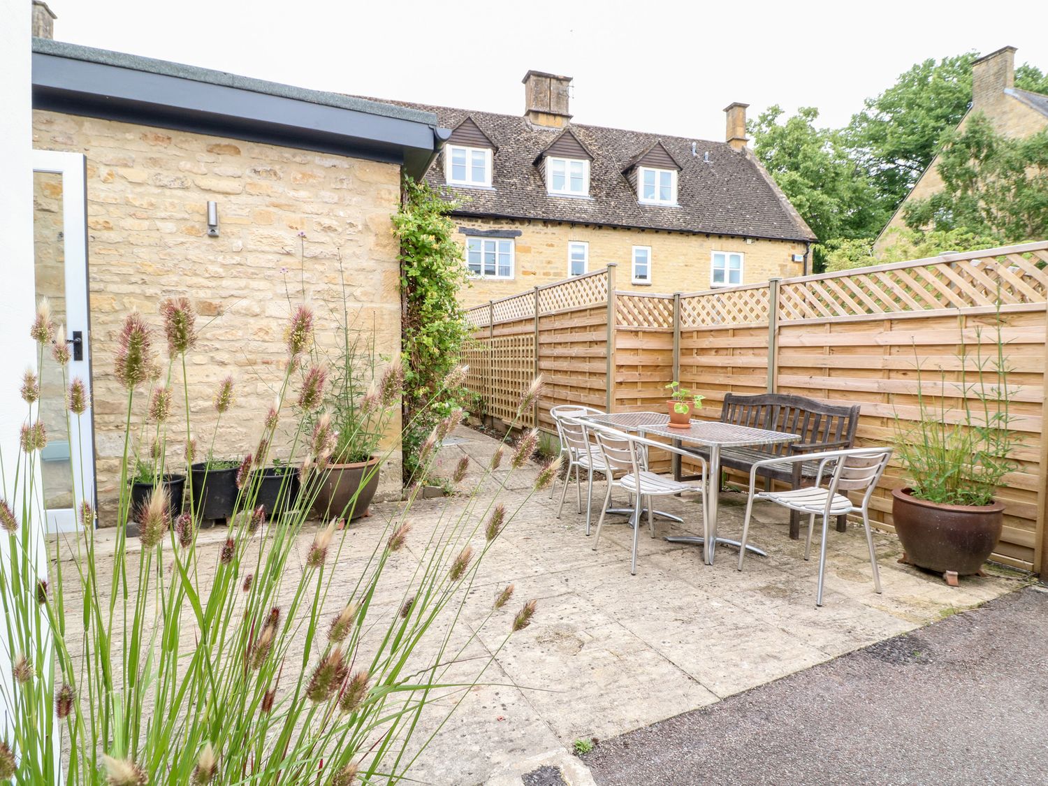 An outdoor patio area with a table and chairs next to a wooden fence and stone buildings at Ruskin House in Moreton-In-Marsh
