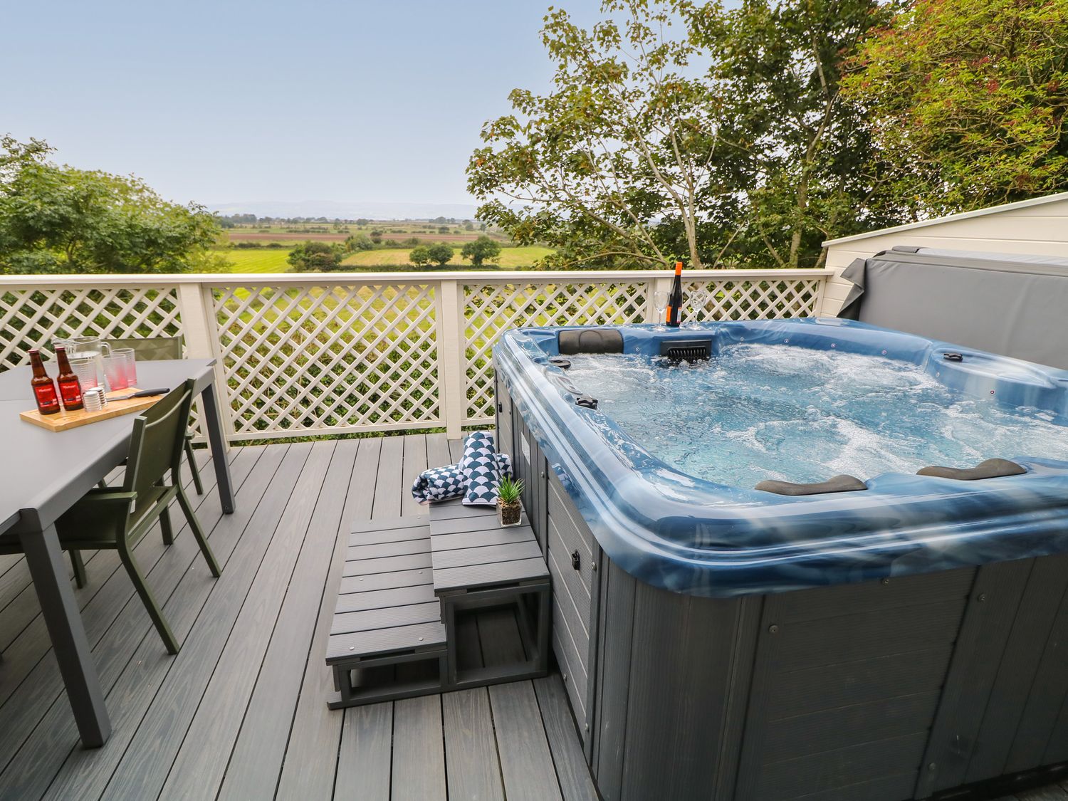 An outdoor deck with a hot tub table with drinks and chairs and a rural view at Old Shop Cottage in Limavady