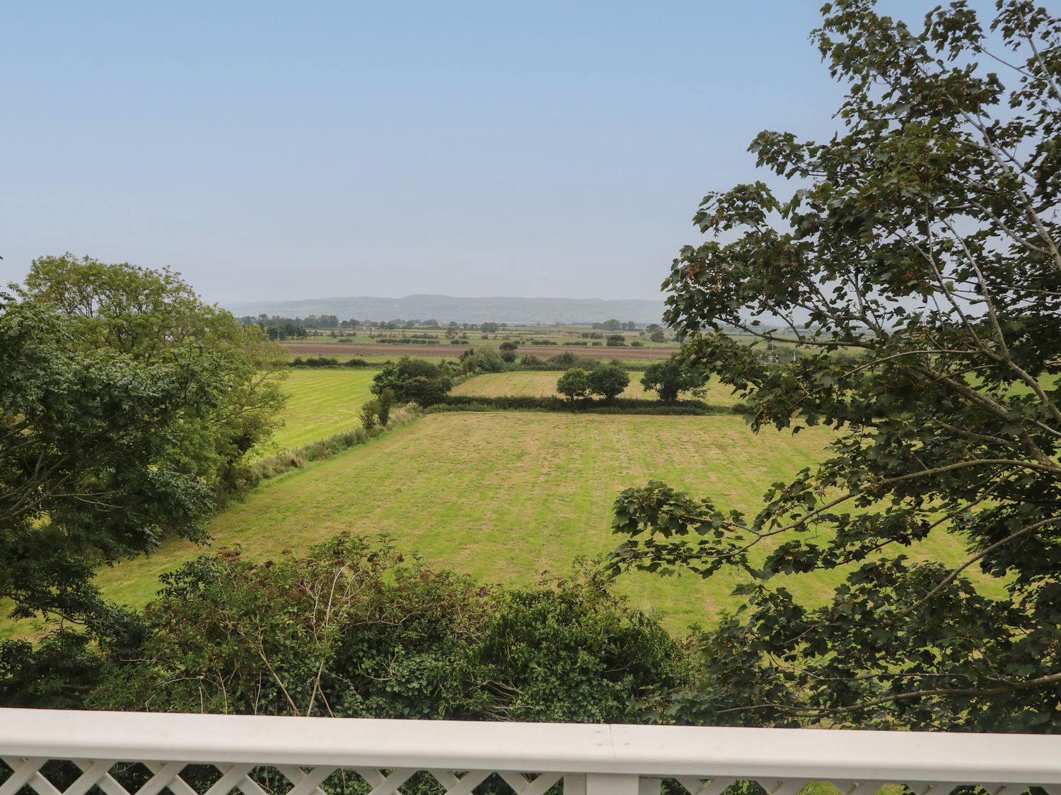 A view of green fields and trees with hills in the background from a balcony at Old Shop Cottage in Limavady