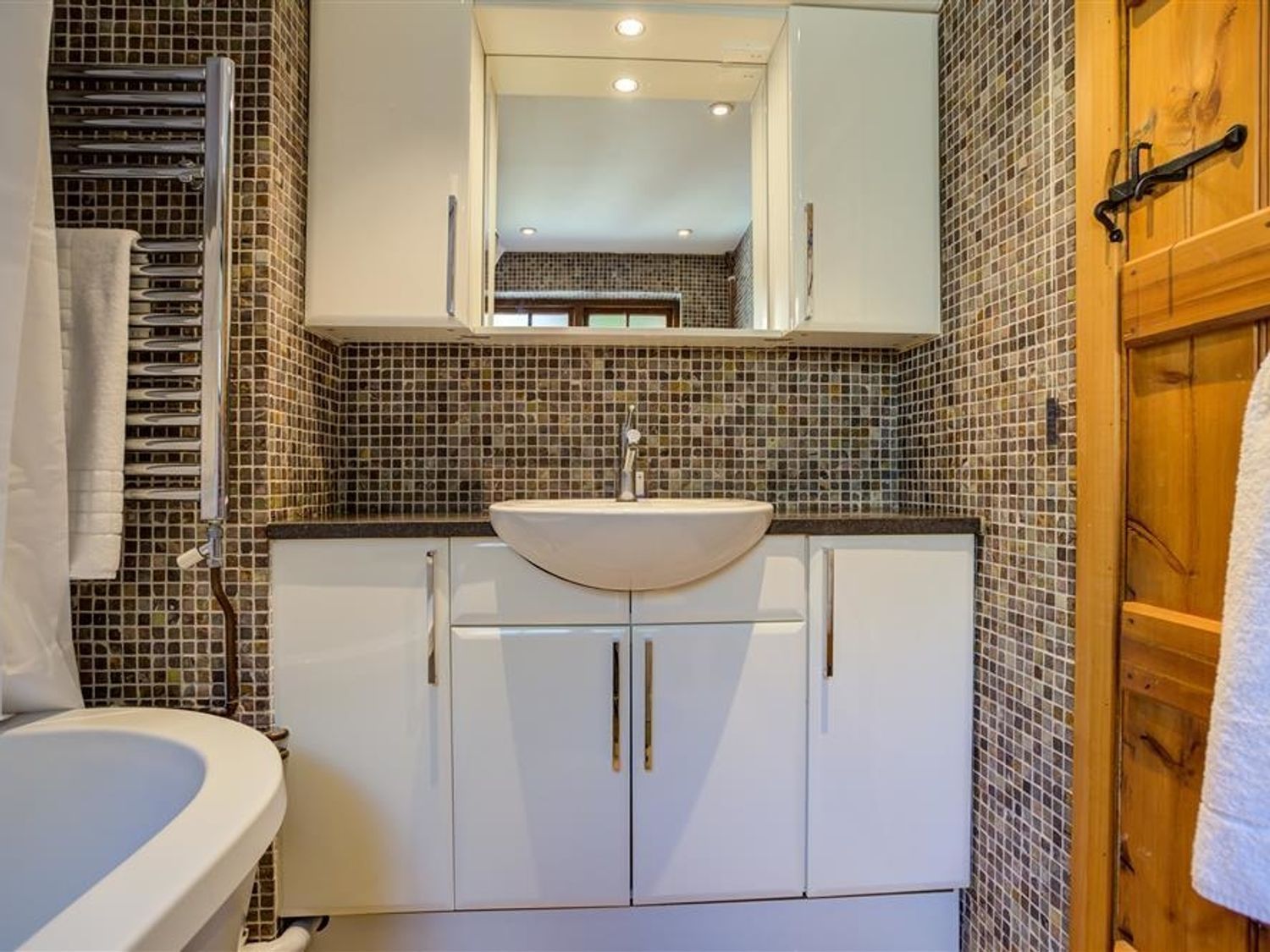 A bathroom with a white sink and cabinets a mosaic tile backsplash a wooden door and a towel rack at Hollytree Cottage in Hook Norton