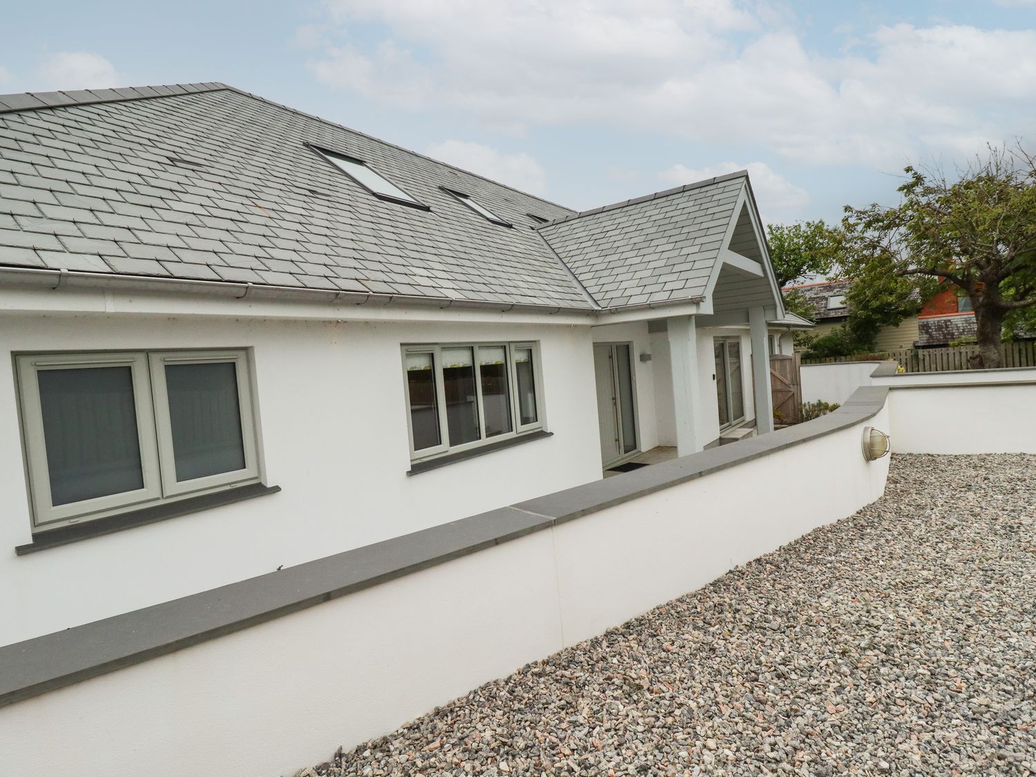 An exterior view of a house with a sloped roof skylights multiple windows a gravel area and a low wall at Woodlands Close in Padstow