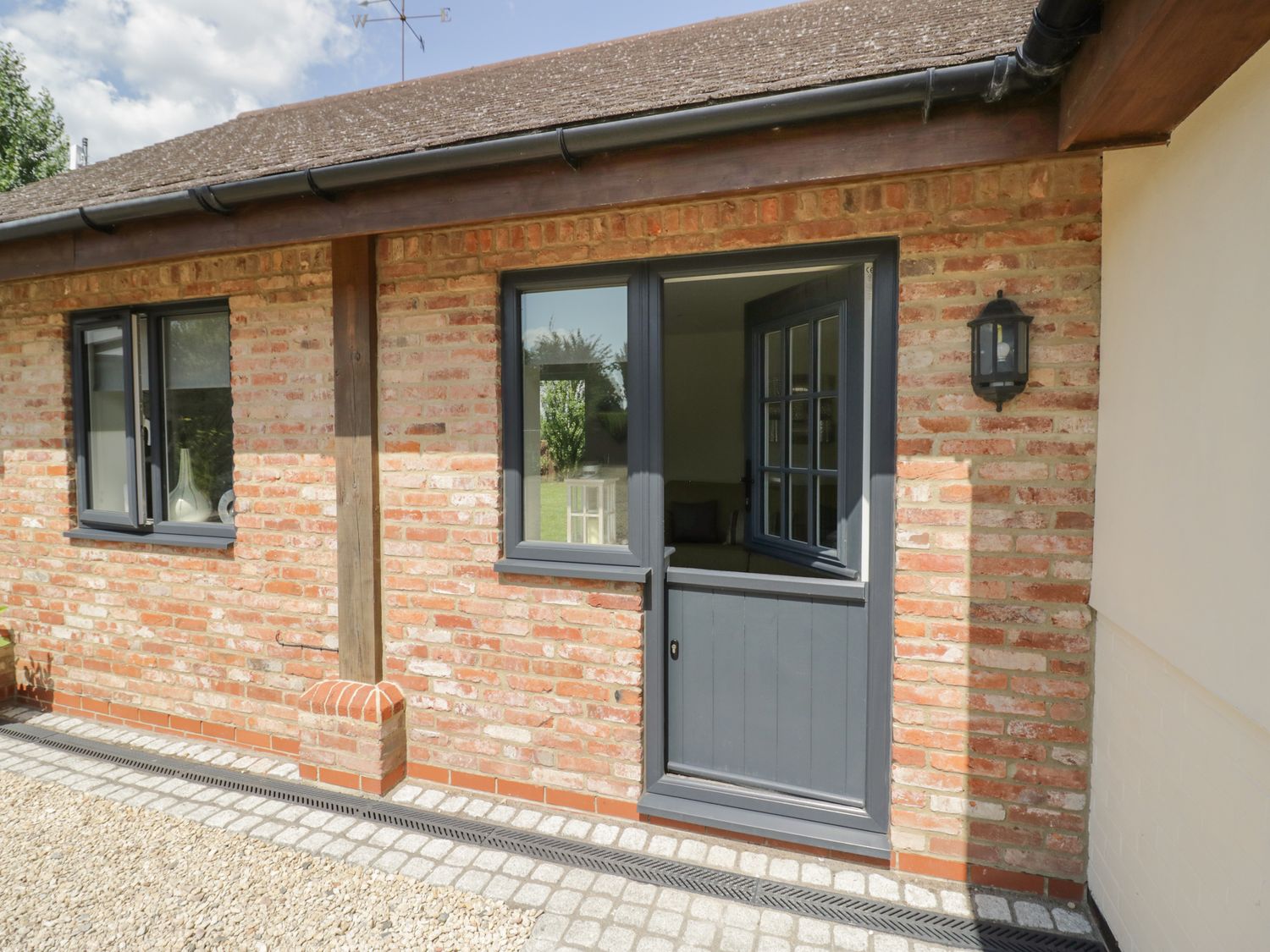 A brick exterior wall with a blue door and two windows at Garden Cottage in Upton Upon Severn