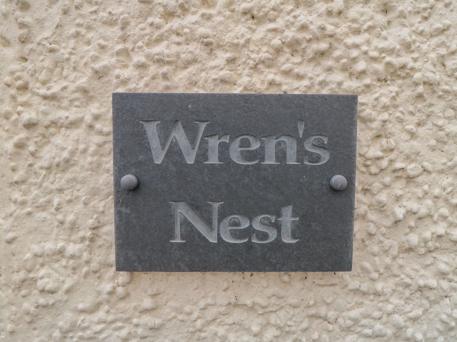 A dark grey sign with the words Wren's Nest mounted on a textured beige wall at Wrens Nest in Thirsk
