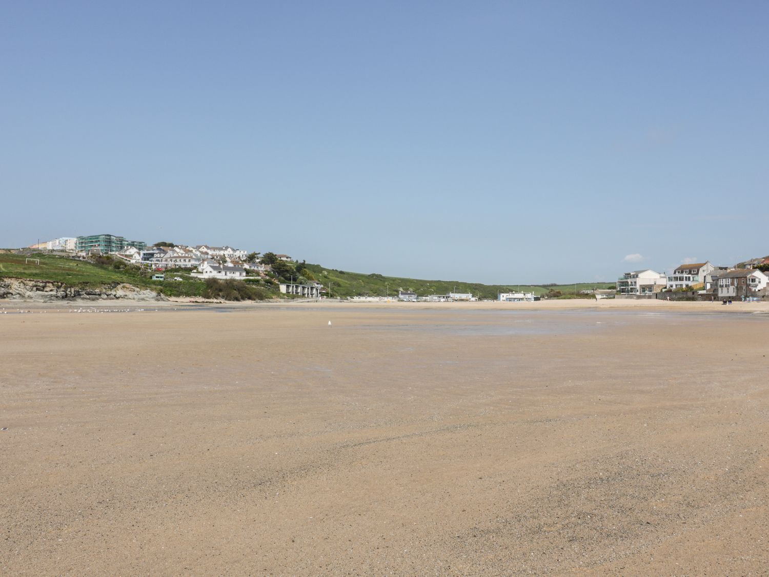 A sandy beach with houses and green hills in the background at Porth Cove in Porth