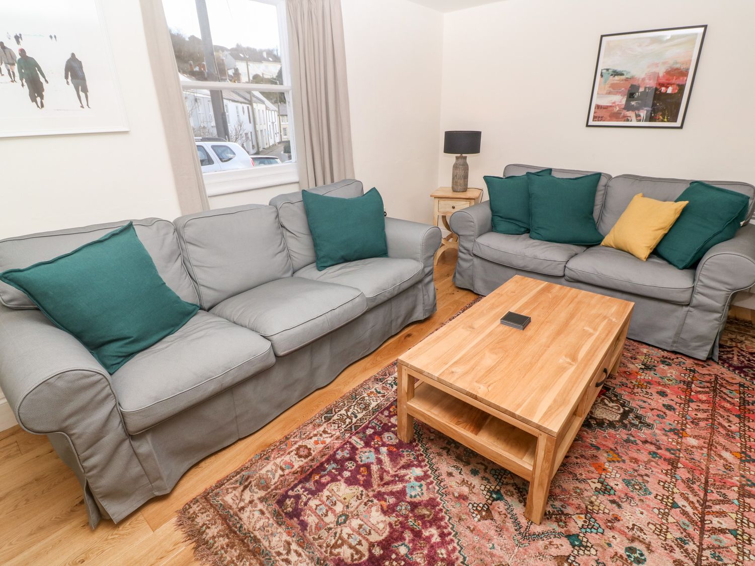 A living room with two grey sofas with green and yellow cushions a wooden coffee table a patterned rug and wall art at Widgeons Keel in Flushing