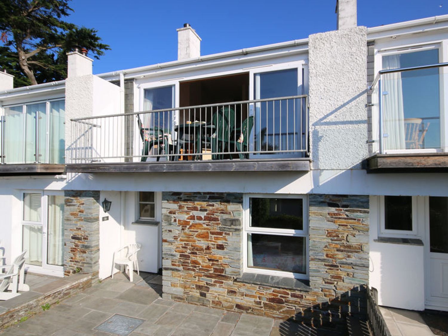 A two-story building with stone and white walls and a balcony with green chairs at Slipway 10 in Rock